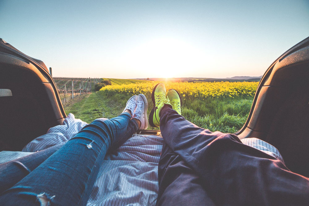 A couple pair of legs layed on grass and pointing to the horizon at sunset.